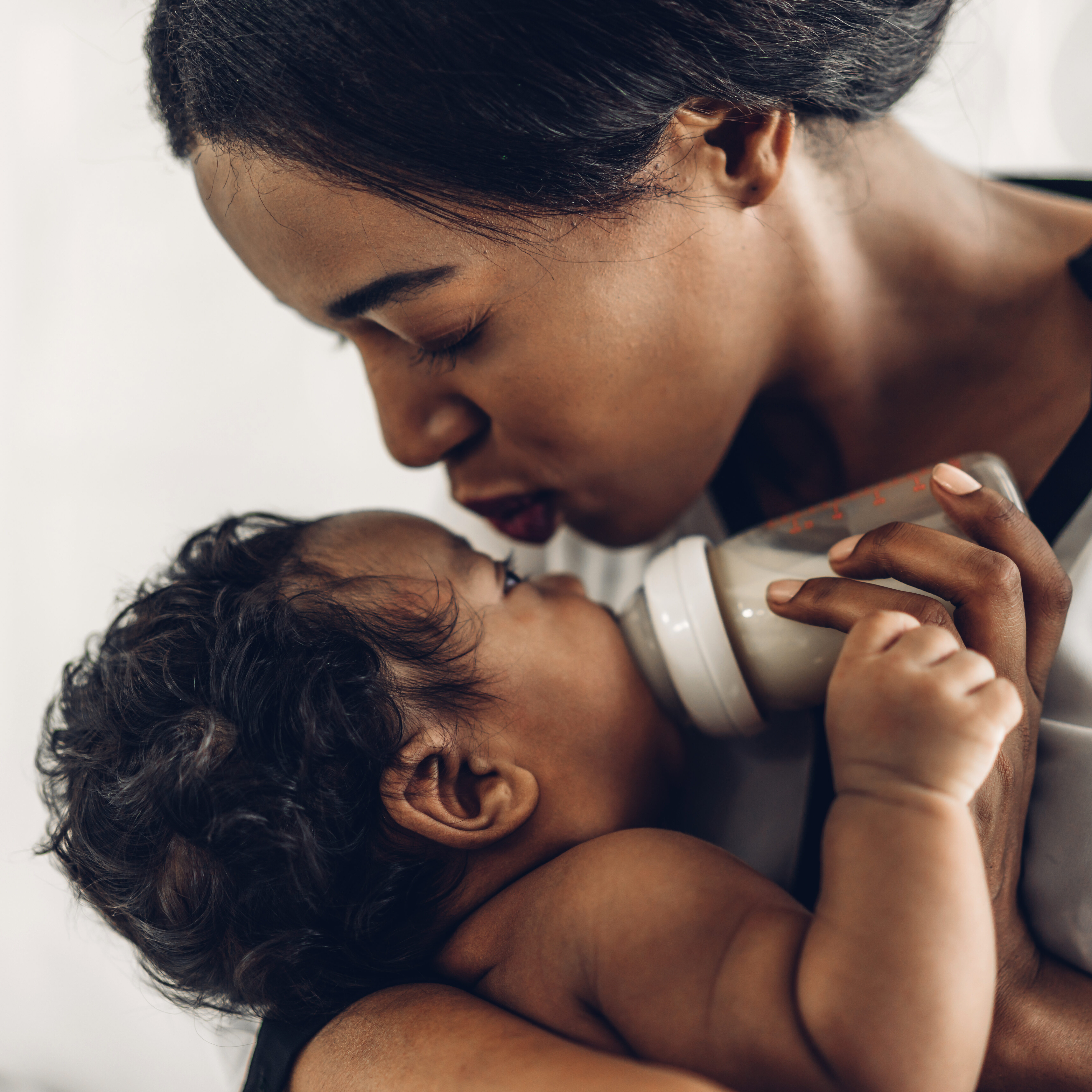 Portrait of enjoy happy love family african american mother playing with adorable little african american baby.Mom feeding bottle of milk to baby cute son in a white bedroom.Love of black family concept